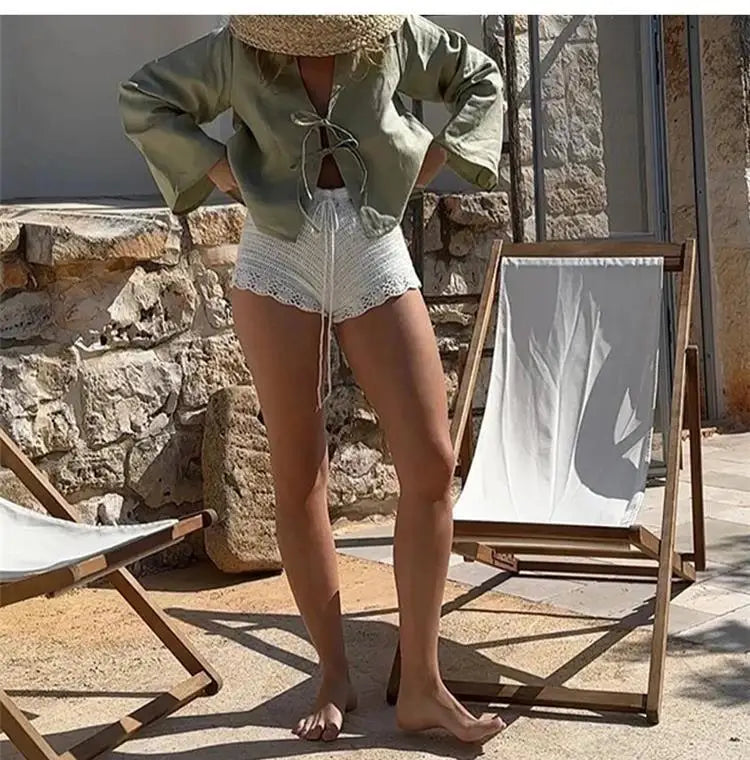 Female model in green linen lace-up V-neck top with long sleeves, standing outdoors by deck chairs.