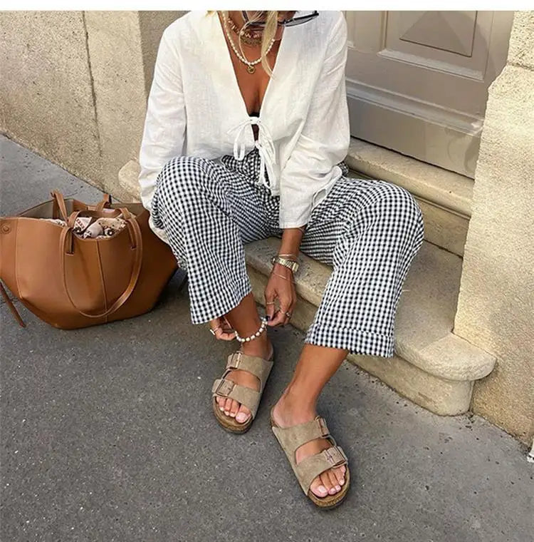 Casual white lace-up V-neck blouse with black and white checkered pants, accessorized with sandals and a brown tote bag.