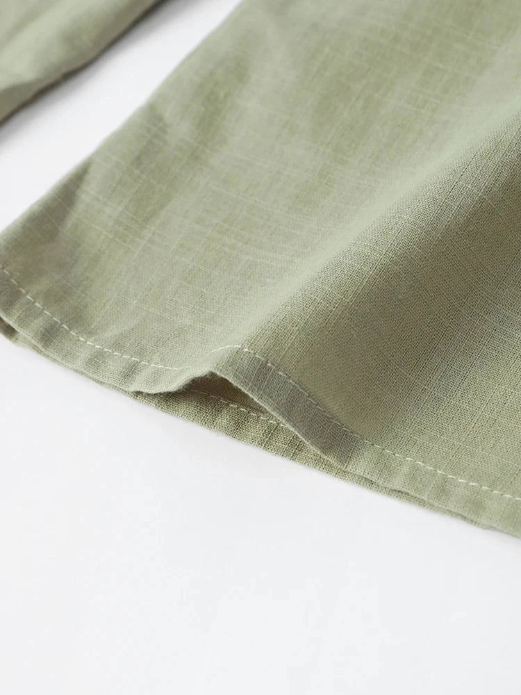 Close-up of lightweight, green cotton linen fabric for women's V-neck long sleeve top, showcasing hem stitching detail.