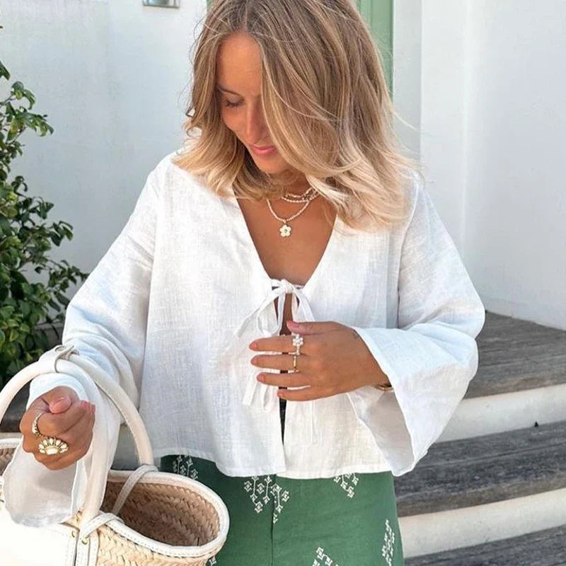 Woman wearing a white cotton linen V-neck blouse with lace-up detail and flare sleeves, spring fashion 2024.